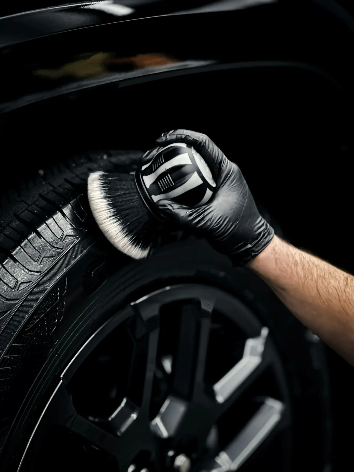 Gloved hand cleaning a car tire with a brush